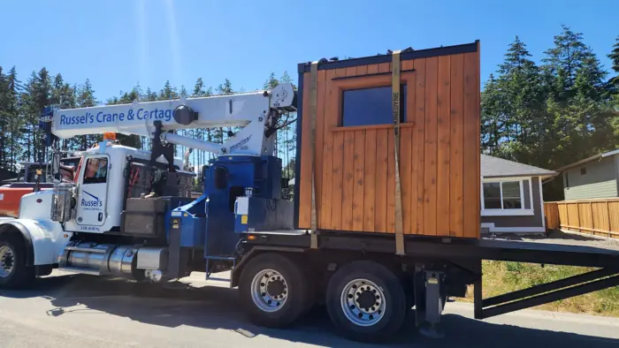 Crane setting a small timber building onto a site
