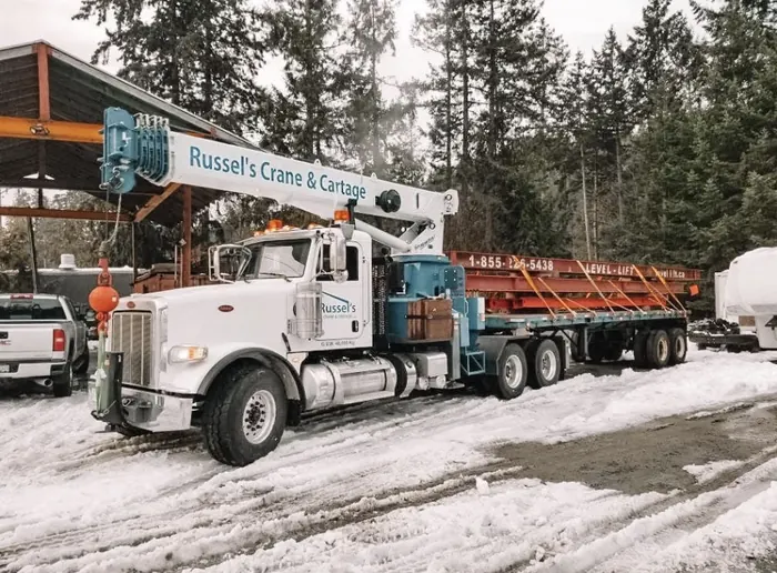 Crane truck with a flatbed of red steel in the snowy yard