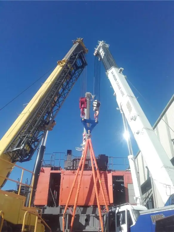 Two cranes lifting a red load between buildings